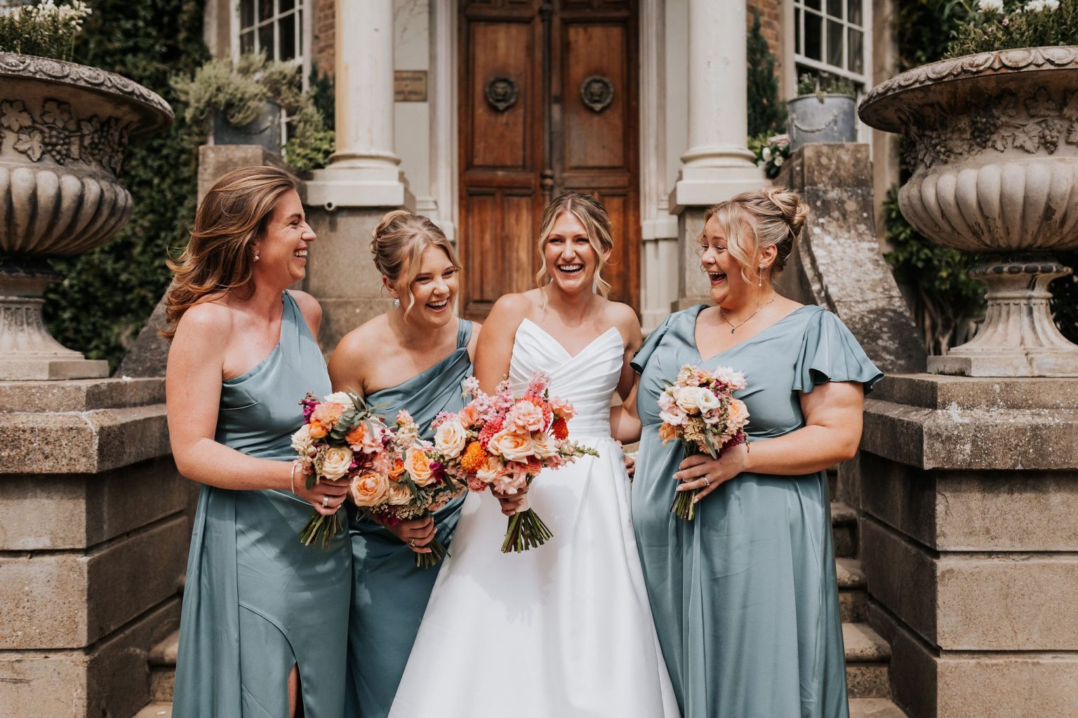 Bride laughing with her three bridesmaids on the steps of the venue