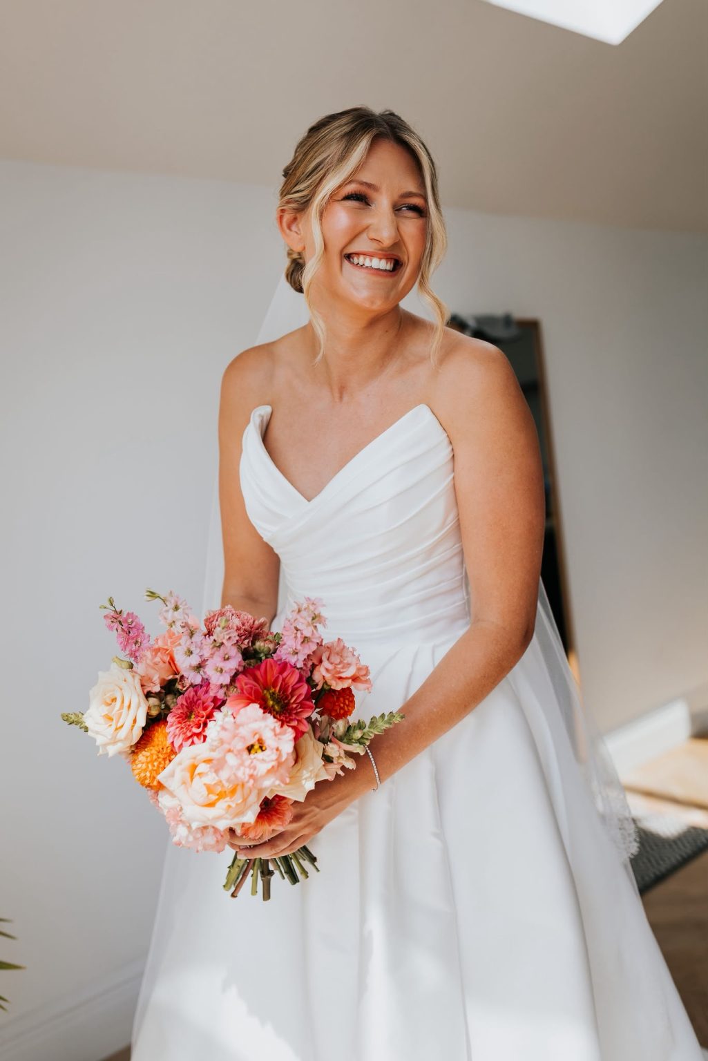 Laughing bride holding a bright bouquet with glowing bridal makeup