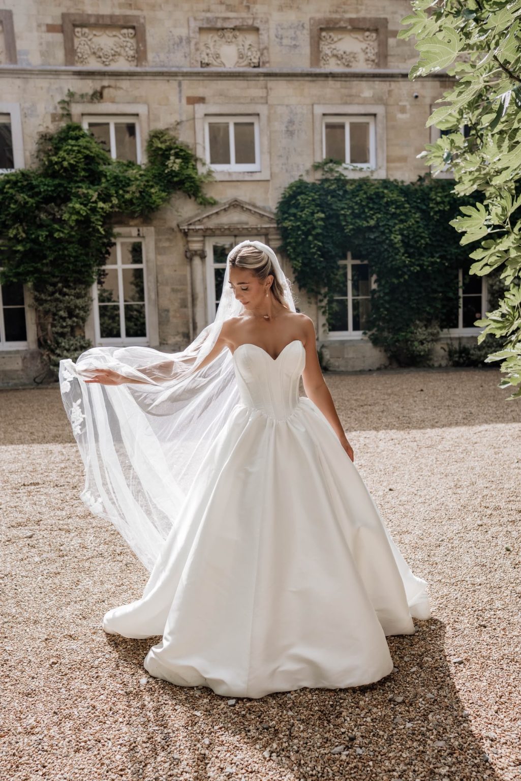 Bride holding out her cathedral veil in a sunlit courtyard